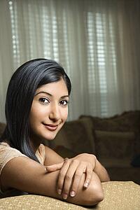 Close up portrait of Asian/Indian young woman sitting on couch.