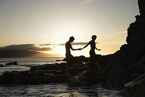 Young adult Caucasian male and female silhouetted on beach.