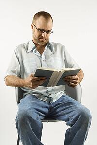 Caucasian man sitting in chair reading book against white background.