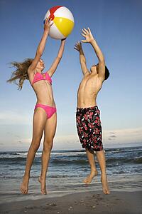Caucasian pre-teen girl and boy playing with beachball on beach.