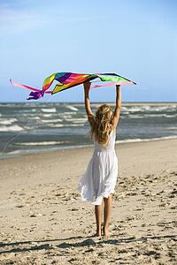 Caucasian pre-teen girl holding kite on beach.
