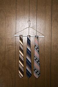 Three retro ties hanging on a wire hanger against wood paneling.