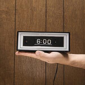 Caucasion male hand holding retro clock set for 6: 00 against wood paneling.
