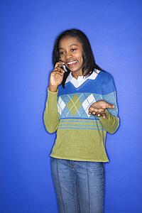 Portrait of African-American teen girl smiling and talking on cellphone standing in front of blue background.