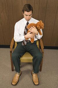Mid-adult Caucasian male sitting in chair holding a stuffed animal looking sad.