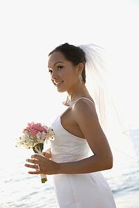 Young adult female Caucasian bride holding bouquet on beach.