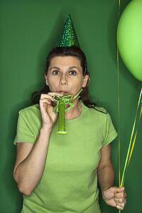 Adult female wearing party hat and blowing party puffer.
