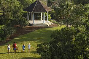 Caucasian family of four walking in park carrying picnic basket.