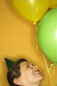Caucasian prime adult female wearing party hat with balloons.