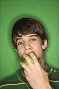 Portrait of Caucasian teen boy biting apple. 