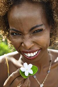 Portrait of mid-adult Black female squinting and holding jasmine flower.