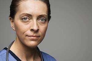 Head shot portrait of Caucasian woman doctor against gray background.