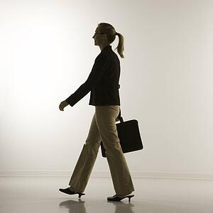 Silhouette of mid-adult Caucasian businesswoman walking and carrying briefcase.