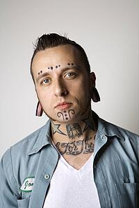 Caucasian mid-adult man with tattoos and piercings.