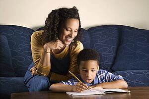 Portrait of young boy doing homework while mother looks over shouulder.