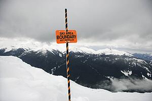 Ski area trail boundary sign with mountain landscape in background.