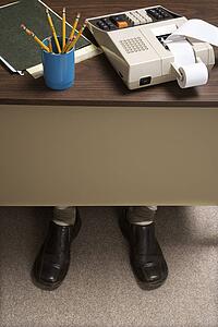 Feet of retro businessman sticking out of bottom of desk with notebook, pencils and adding machine.