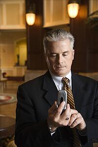 Caucasian prime adult male businessman dialing cellphone in hotel lobby.