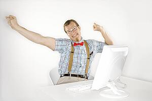 Caucasian young man dressed like nerd stretching arms out and happy in front of computer.