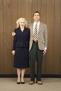 Mid-adult Caucasian male in retro suit with arm around mid-adult Caucasian female.