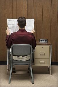 Back view of retro businessman sitting at desk reading paper.