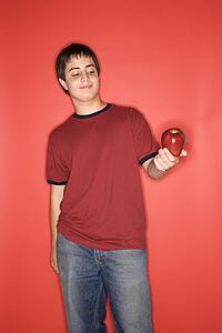 Portrait of Caucasian teen boy holding an apple standing against red background.
