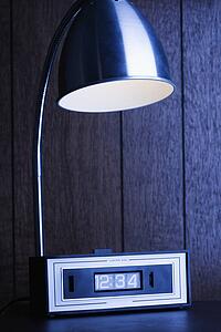 Desk lamp shining down on retro clock against wood paneling.