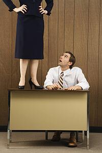 Mid-adult Caucasian male sitting at desk looking up to Caucasian female standing on desk.