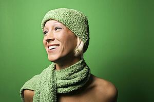 Portrait of smiling young adult Caucasian woman on green background wearing winter hat and scarf.