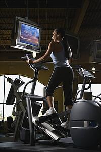Prime adult Caucasian female on elliptical machine at gym.
