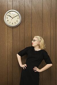 Mid-adult Caucasian female in vintage outfit looking up at clock on wall.