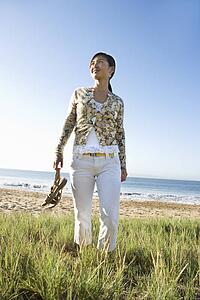 Young Asian female walking down beach carrying sandals.