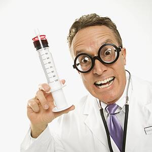 Mid-adult Caucasian male doctor wearing eyeglasses holding an oversized syringe.