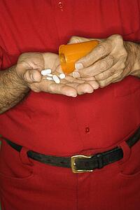 Mature adult Caucasian male emptying pill bottle into hand.