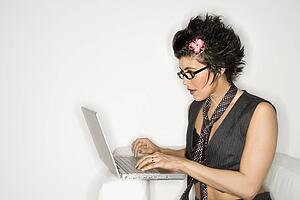Trendy Hispanic woman typing on laptop against white background.