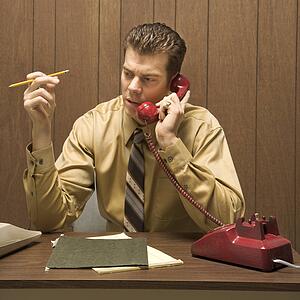 Caucasion mid-adult retro businessman sitting at desk talking on telephone.