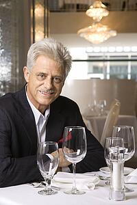 Caucasian mature adult male sitting at restaurant table looking at viewer smiling.