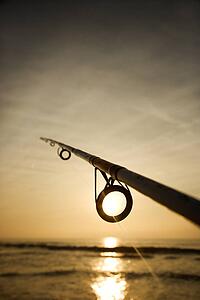 Fishing pole against ocean at sunset.