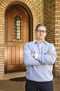 Caucasian adult male standing with arms crossed near arched doorway. 