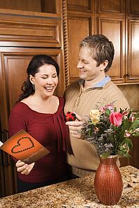 Caucasian man giving Caucasian woman card, present and flowers.
