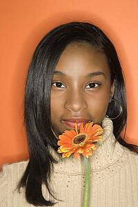 Portrait of African-American teen girl holding single Gerbera Daisy against orange background.