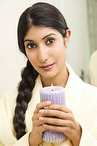 Close up of Asian/Indian young woman holding lit candle looking at viewer.