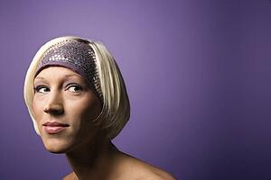 Head and shoulder portrait of bare young adult Caucasian blond woman on purple background wearing headband.