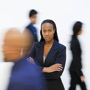 African-American businesswoman standing with arms crossed while others walk by.