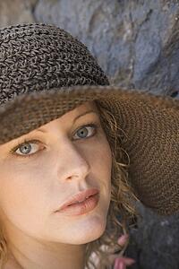 Close-up of young adult female Caucasian by rock wearing brimmed hat.