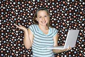 Young Caucasian woman holding laptop shrugging and smiling.