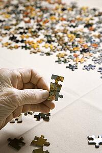 Close-up of Elderly Caucasian woman's hand holding puzzle piece.