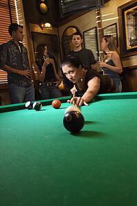 Young caucasian woman preparing to hit pool ball while playing billiards.