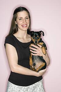 Smiling Caucasian woman holding Miniature Pinscher dog standing against pink background.