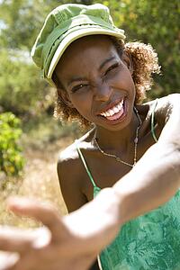 Mid-adult Black female smiling with hand reaching out towards camera.